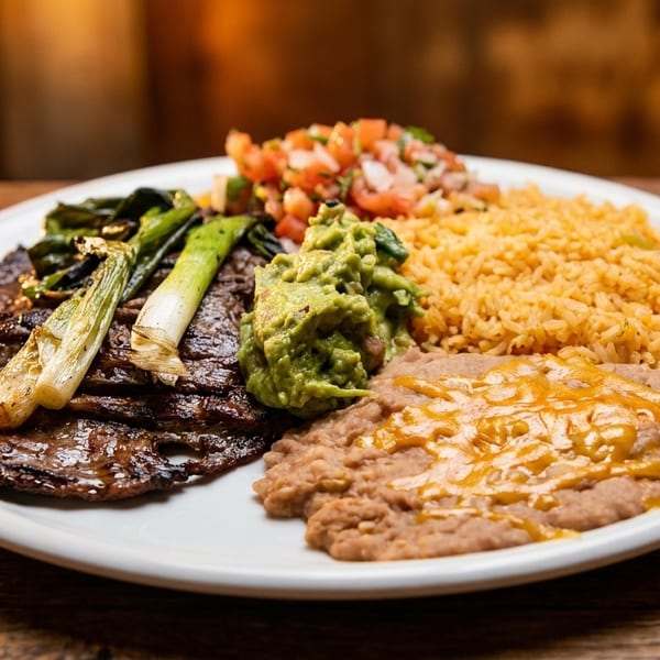 Carne asada with grilled green onions, guacamole, pico de gallo, rice, and refried beans.