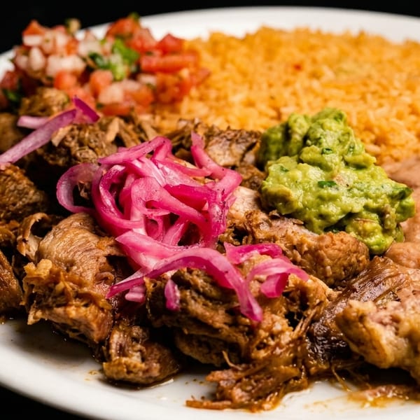 A plate of carnitas with pickled red onions, rice, refried beans, guacamole, and pico de gallo.