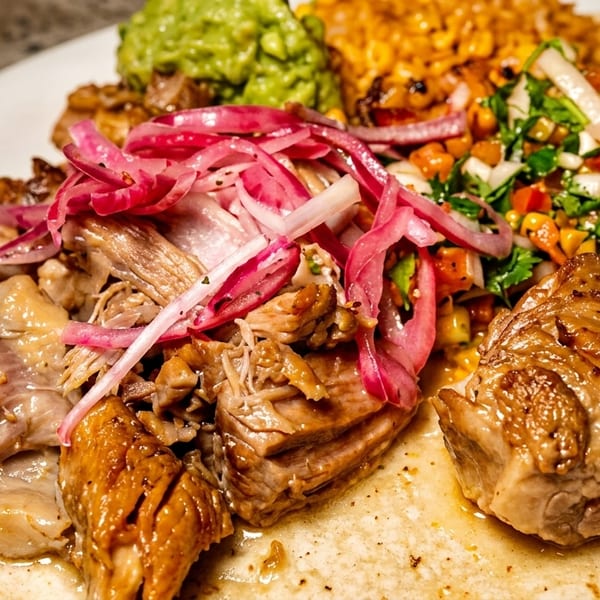 Close-up of a taco with carnitas, pickled red onions, guacamole, and corn salsa on a white plate.