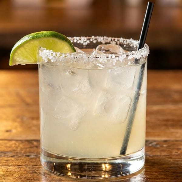 A margarita with a salted rim, lime wedge, and black straw on a wooden table.